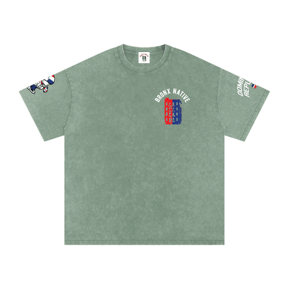 Sage green Bronx Native tee with red and blue building graphic, sleeve prints, and streetwear style design
